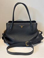 Front view of handbag on flat surface showing top handles and detachable strap