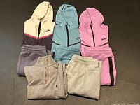 Overhead view of all eight pieces laid out: three hoodies, four pairs of sweatpants, one sweater