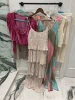 All 5 dresses and tops hanging on hanger against white wall showing full length and variety of colors.