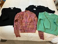 Four sweaters laid flat on white background showing black knit, pink-orange Dex cardigan, green knit, and black square neck sheer sleeved sweater