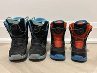 Front view of two pairs of youth snowboard boots, blue size 3K and orange size 12C, showing their toe area and lace systems.