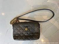 Full view of the bag with gold chain and leather strap, laid flat on a light surface