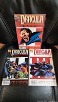 Three comic books bearing the Marvel logo, titled Dracula Lord of the Undead, displayed on a black leather chair. Shows issues #1, #2, and #3 with colorful, detailed covers of Dracula and vampire scenes.