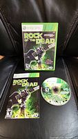 Front cover of Rock of the Dead Xbox 360 game case, manual, and disc displayed on black chair.