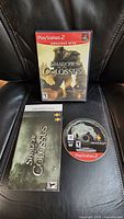 Front view of the PS2 game case showing the cover art of Shadow of the Colossus Greatest Hits edition, along with the manual and game disc placed on a chair.