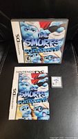 Photo showing original case, instruction manual, and game cartridge for The Smurfs Nintendo DS game on a black surface.