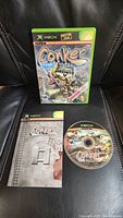 Front view of game case, manual, and disc showing Conker character and Xbox branding.