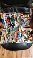 Full lot of 40 vintage comic books displayed together on a chair, showing colorful spines and covers including Thor and other titles.