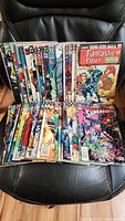 Photo showing multiple comic books including Fantastic Four, Superboy and others stacked in two rows on a black chair.