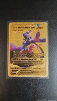 Front view of the gold foil Mewtwo & Mew GX Pokemon card in protective sleeve showing main artwork and text details.
