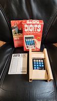 Photo of Coleco Digits game, original box and instruction sheet displayed on black surface.