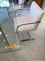 Side view of one white upholstered armchair with chrome cantilever frame beside a glass table