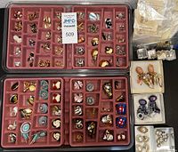 Overview of multiple trays and boxes containing a variety of clip on earrings, pierced earrings, a brooch, and a necklace.
