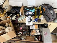 Overview of assorted items showing wooden reels with rope, sewing box, drawing instruments, and other hardware on a desk surface.