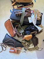 Overview of assorted leather cases, holsters, belts, and accessories piled together showing condition and variety.