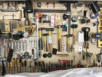 Overall view of pegboard holding wrenches, hammers, screwdrivers, heater, gloves, tape and other tools.