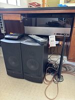 Harman Kardon receiver with two Infinity RS3 speakers, portable CD player, remote control, wires and cords underneath wooden desk.