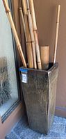 Side view of a tall rectangular ceramic planter with bamboo sticks inside, showing glossy earth-tone glaze with imperfections.