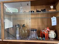 Cabinet shelf with glass pumpkin, crystal figurines, ceramic vase, Dala horse, ceramic pitcher, and small decorative items