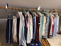 Wide view of approximately five feet of hanging women's clothing, showing various skirts, blouses, and pants arranged on hangers.