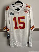 Front view of the white Patrick Mahomes #15 football jersey with Super Bowl LIV and Chiefs patches, still hanging on a black hanger showing tags and size XL.