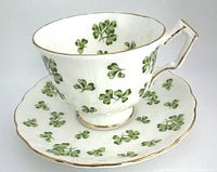 Front and side view of Aynsley Shamrock teacup on matching saucer showing shamrock pattern and gold trim.