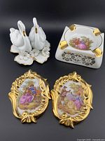 Alta Ceramiche swans figurine, Limoges ashtray, and two miniature Limoges wall plaques with detailed gold-gilded frames and painted romantic scenes shown together