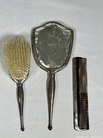 Top view of front sides of hand mirror, hairbrush, and comb showing reflective and bristle surfaces.