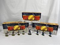 Three boxed sets displayed with painted miniature figures in front, showing the packaging and opened contents.
