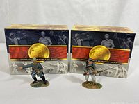 Two boxed miniature figures in front of matching boxes labeled 'Miniatures for the Ages' with gold emblem.