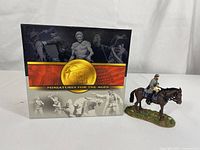 Photo of the product packaging with the miniature figure positioned beside it.