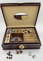 Open brown handmade jewellery box showing a variety of cuff links and tie pins organized within the compartments and more pairs outside the box.