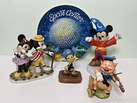 Photo showing five Disney character figurines and the Epcot Center plate with blue background featuring the 1982 iconic Epcot ball.