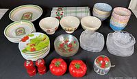 Photo showing all items in the lot including ceramic bowls, glass plates, vegetable-themed salad plates, and red tomato salt and pepper shakers.