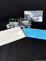 Die-cast model of 1907 Rolls-Royce Silver Ghost with original documents and brochures included, all displayed on black background.