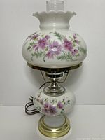 Full view of the electric hurricane lamp showing painted floral design on shade and base, metallic stand and base, and electrical cord.