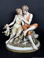 Front angle of porcelain figurine showing young couple sitting with cherub on a detailed naturalistic base.