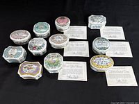 Overview of all 11 decorated porcelain music boxes with matching certificates of authenticity arranged on black background