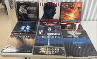 LaserDisc lot displayed on table showing nine movie titles: Schindler's List, Mission Impossible, Deep Impact, two copies of The Abyss, Twister, Dante's Peak, Independence Day, Escape from New York.
