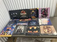 Overall view of 14 LaserDiscs arranged on a table, showing cover art for Batman Returns, Jurassic Park, Dick Tracy, The Witches, Roger Rabbit, Casper, Indiana Jones, Home Alone and others
