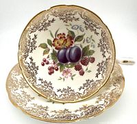 Top view of teacup and saucer showing fruit, berries, and flower design with ornate gold trim
