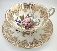 Front angle view of teacup sitting inside saucer showcasing interior fruit and flower design with gold trim