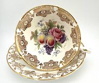 Close-up image of Paragon teacup resting on matching saucer showing detailed floral fruit and rose design with gold rim accents.