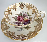 Front angle of Paragon teacup and saucer showing floral and fruit pattern with gold detailing