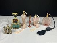 Seven vintage art glass perfume bottles arranged in a row on white surface against black background. Various shapes including butterfly and geometric designs, some with atomizers.