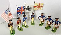 Front view of six painted metal soldier figurines including flag bearers and drummers on green bases in Prussian uniforms.