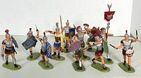 Front view of all 11 Roman legionary plastic toy soldiers arranged in loose formation showing various poses and colors of shields and helmets.
