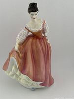 Porcelain figurine of a woman in a coral pink gown holding up her skirt, showing detailed features and design.