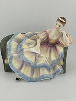 Front and side views of Royal Doulton Pauline figurine seated on a dark green sofa chair showing detailed dress and posture.