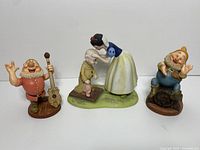 Snow White figurine bending to kiss Dopey on a green base, Dopey's head and base re-glued, with Happy dwarf holding a guitar and Cheerful Leader dwarf sitting on a barrel beside them.